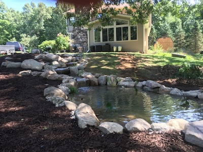 Water feature pond, surrounded by rocks. The pond is built near a house.