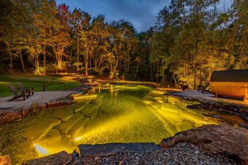 Swim pond with outdoor ligthting. The area is surrounded by lots of trees.