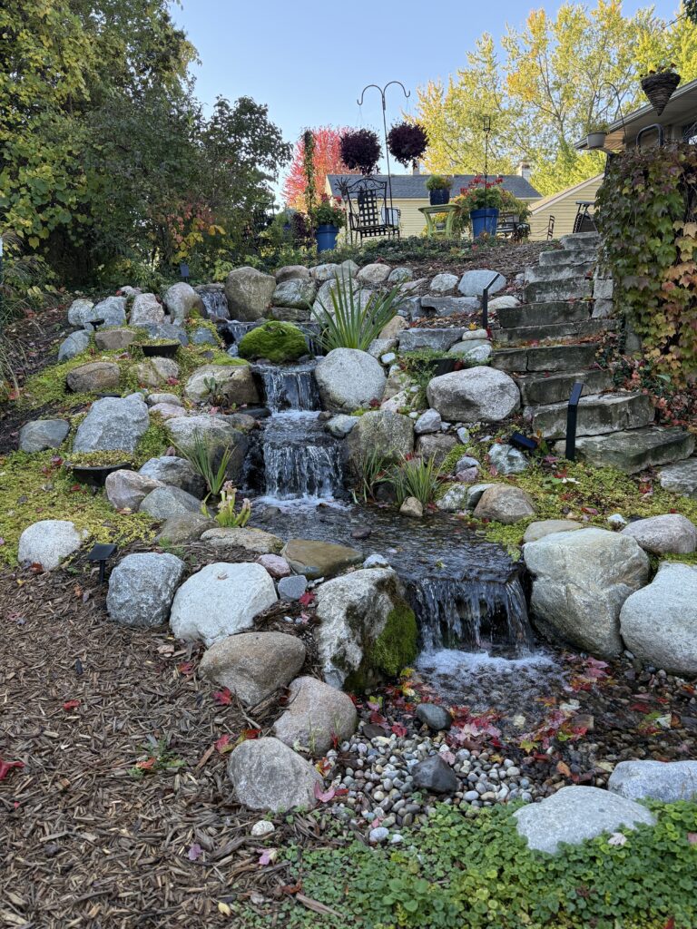 Pondless backyard waterfall with surrounding plants next to a stone steps