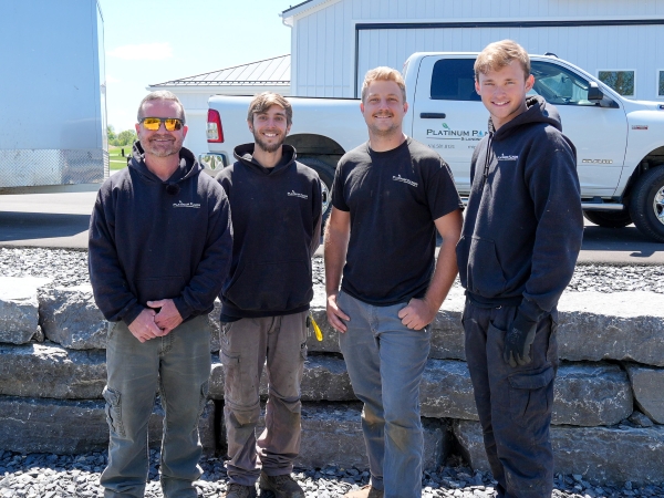 Four men posing outdoors, smiling.