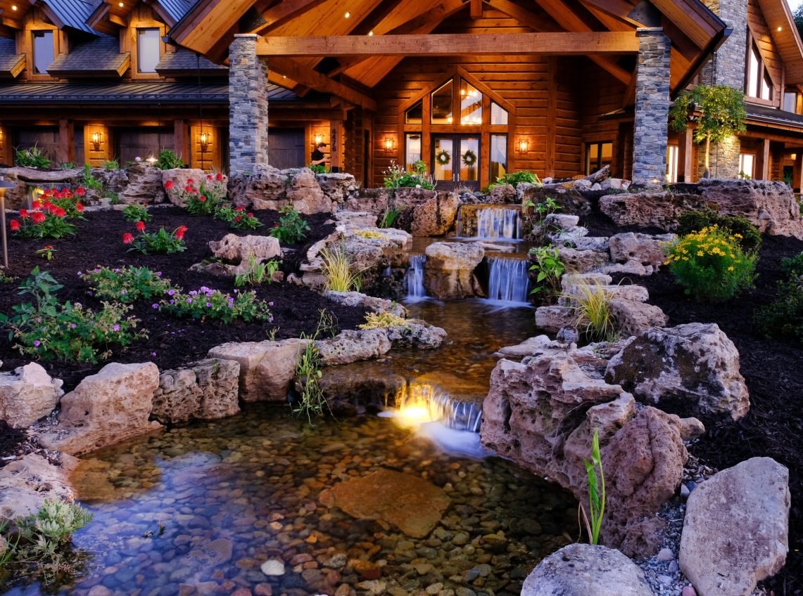 Multi-layer waterfall with plants and outdoor lighting Multi-layer waterfall with pond, landscaping, and outdoor lighting.